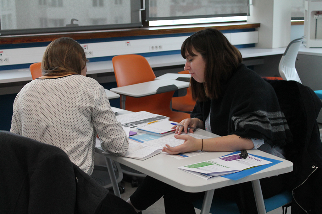 Deux femmes consultent des documents autour d'une table dans une salle de cours
